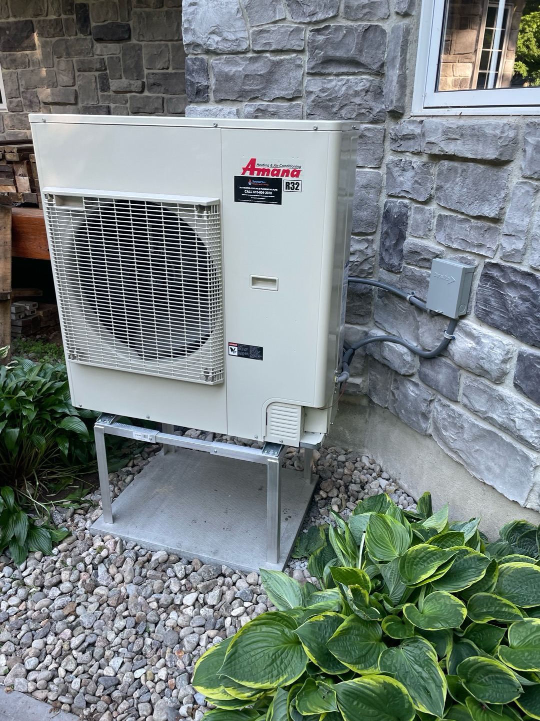 An Amana heat pump on a stand beside a stone house